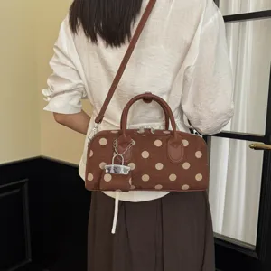 Detail view of a stylish brown polka dot handbag worn on the shoulder, featuring a cute lock charm.