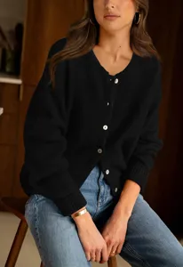 Detail view of a black knit cardigan with white buttons, worn by a model in a cozy interior.