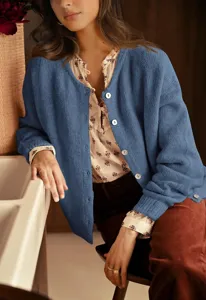 Detail shot of a cozy blue knitted cardigan with buttons worn by a model in a warm room.