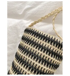 Nahaufnahme der schwarz-weißen gewebten Strohtasche mit feiner Textur und geflochtenem Riemen.