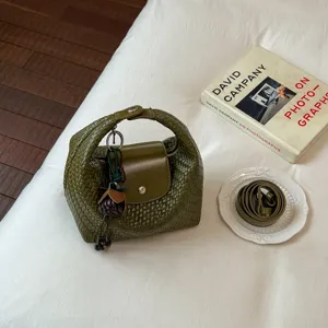 Green woven dumpling bag with strap and pendant, stylish shoulder bag for women.