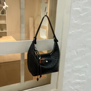 Detailed view of black woven leather shoulder bag, hobo dumpling bag with flap and chic charm.