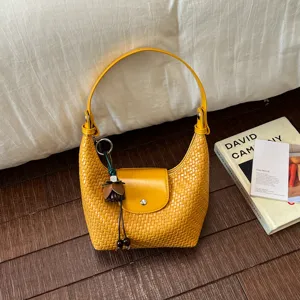 Detail shot of a yellow woven hobo shoulder bag featuring a front flap and chic pendant charm.