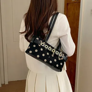 Dettaglio della borsa a spalla nera con pois ed elegante cintura con anelli metallici.