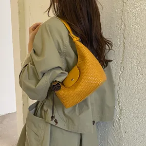 Close-up detail of stylish yellow woven shoulder hobo bag with flap and knot pendant.