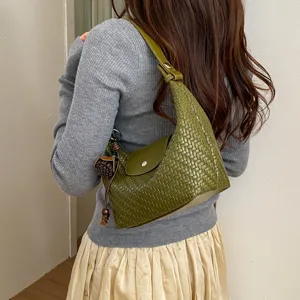 Green woven leather underarm shoulder bag, detailed view showing texture, flap and charm.