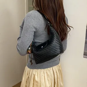 Woven leather shoulder bag detail view, black dumpling hobo purse with flap closure and charm.