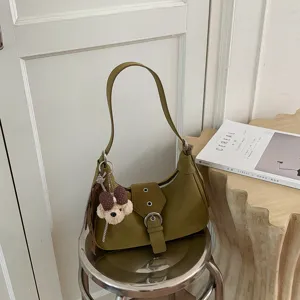 Detalle de bolso bandolera verde, elegante tira con hebilla y bonito colgante de osito.