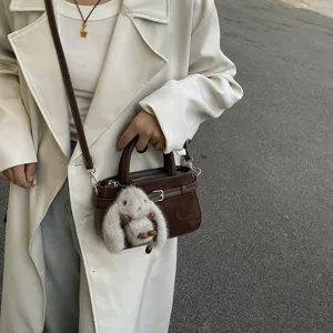 Detail view of retro brown crossbody mini bag with cute plush rabbit charm and trench coat.