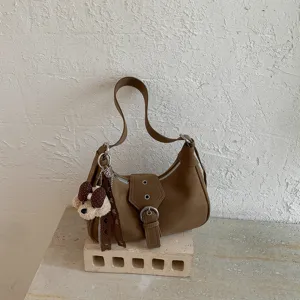 Vista detallada del bolso de hombro marrón estilo coreano con dije de oso y hebilla.