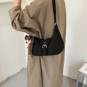 Vista detallada del bolso de hombro negro con hebilla de metal y lindo colgante de oso.