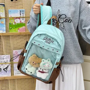 Dettaglio di uno zaino azzurro a pois con tasca frontale trasparente e peluche decorativi.
