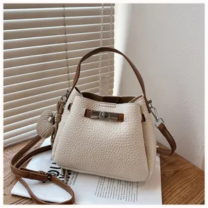 Gros plan d'un sac seau blanc élégant avec détails marron et charm tricoté sur table.