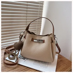 Vue détaillée d'un sac seau beige avec poignée marron, fermoir tourniquet et charm cœur tissé.