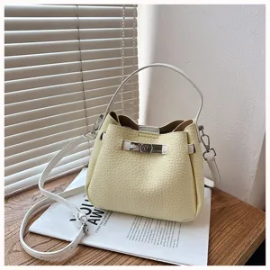 Vue détaillée du sac seau jaune élégant avec poignée blanche, texture grenue et fermoir.