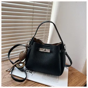 Sac seau noir en cuir texturé avec poignée, fermoir tournant et charmant pendentif en tricot chic.