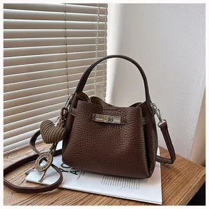 Vue détaillée d'un sac seau en cuir marron texturé avec serrure métallique et pendentif.