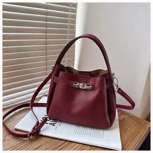 Gros plan sur l'élégant sac seau en cuir bordeaux avec fermoir métallique sur table en bois.
