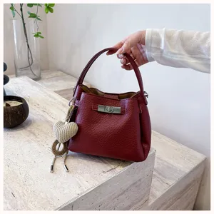 Détail sac à main seau en cuir rouge, fermeture à tour élégante et joli pendentif cœur.