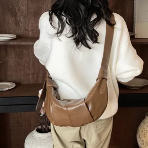 Detail van bruine leren schoudertas in trendy croissantstijl met een brede schouderband.