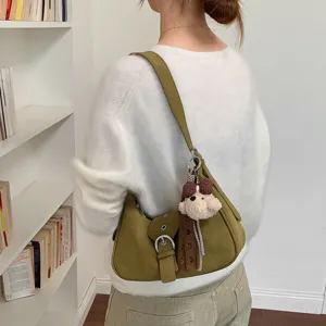 Detalle de bolso de hombro verde con colgante de oso tierno y hebilla de metal.