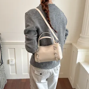 Vista dettagliata della borsa a mano cilindrica beige chic con tracolla e fibbie eleganti.