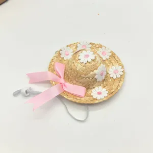 Close-up detail of cute pet straw hat featuring pink ribbon bow and white flower embroidery.