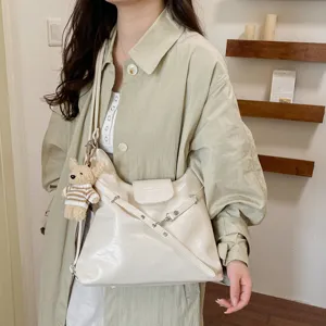 Detalle de bolso de hombro para mujer en suave piel crema con correa cruzada y colgante de oso.