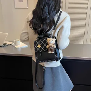 Elegante piccolo zaino nero da donna, con motivo a rombi chic e grazioso ciondolo a forma di orsetto.