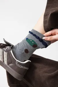 Close-up detail of grey cotton mid-tube socks featuring cute green car pattern and navy ruffle cuff.