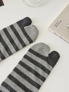 Detail view of grey black striped split toe socks, flat lay styling on white table background.