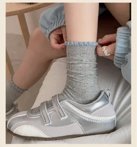 Closeup of gray speckled women socks with blue ruffle cuff and stylish silver sneakers detail