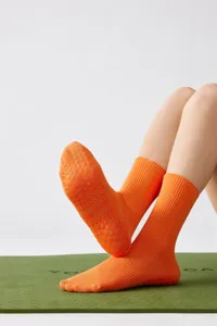 Nahaufnahme von leuchtend orangen Anti-Rutsch-Yogasocken mit Silikonnoppen auf Matte.