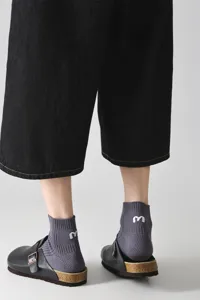 Detailansicht grauer Baumwoll-Kurzsocken mit weißem gestickten Buchstaben M an der Ferse.