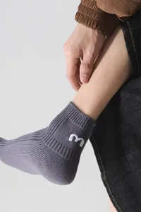 Nahaufnahme grauer Sneakersocken mit gesticktem weißem Buchstaben m, Baumwolle.