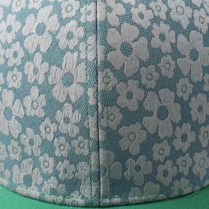 Close-up detail of green baseball cap with silver floral pattern and neat stitching.