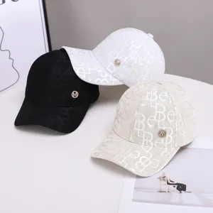 Detailed view of fashionable monogram baseball caps with metal logo in black, white and beige.