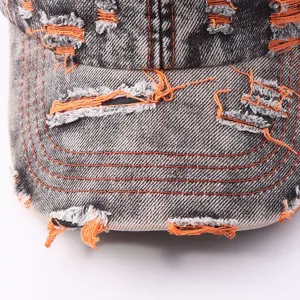 Close-up detail of distressed denim baseball cap brim, washed black with orange contrast.