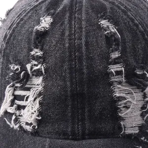 Close-up view of distressed denim baseball cap showing rugged raw edge ripped texture.