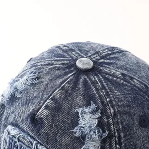 Detailopname van vintage verwassen denim honkbalpet met knop en versleten scheuren en details.