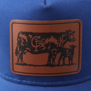 Detalle de la gorra trucker azul con parche de cuero marrón, gráfico de vaca y texto CF.