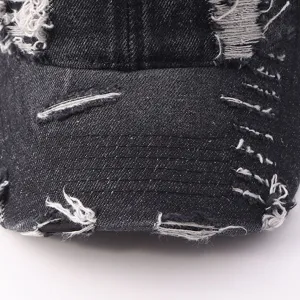 Close-up shot of black distressed denim baseball cap featuring frayed rips and vintage stitch details.