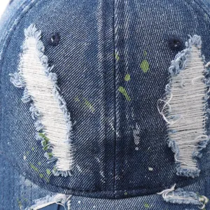 Closeup of distressed denim baseball cap with artistic paint splatter and ripped details.