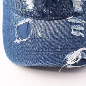 Close-up detail of distressed blue denim baseball cap featuring stylish paint splatter effect.