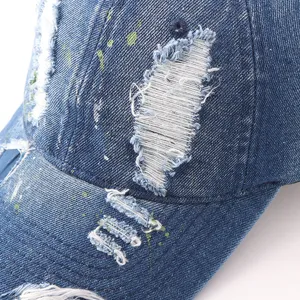 Close-up detail of distressed denim baseball cap with trendy paint splatters and frayed edges.