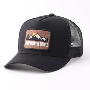 Vista detallada de la gorra trucker negra de malla con parche bordado de montaña y texto.