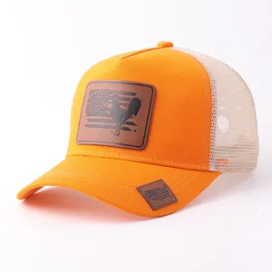 Vista detallada de la gorra trucker naranja de malla con un parche de cuero y bandera.