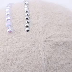 Close-up view of a knitted fur hat detail featuring elegant pearl and rhinestone decorations.