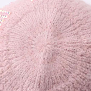 Gros plan sur un bonnet tricoté rose avec texture en laine douce et détails scintillants.