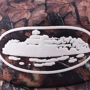 Close-up detail of camo trucker hat featuring white cruise ship embroidered patch design.